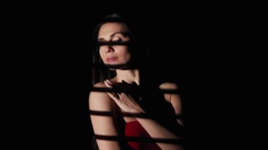 Vücut estetiği yaratıcı reklam konseptinin güzelliği. Stüdyoda kadın modelin portresi. Siyah arka planda kırmızı elbiseli çekici bir kadın. Jalousie 'den gelen ışık kameraya bakıyor..