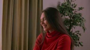 İnsani aşırı duygular yaratıcı reklam konsepti. Çekici kadın modelin olumlu ruh hali portresi. Kırmızı balıkçı yakalı esmer kadın odada oturuyor ve gülüyor..
