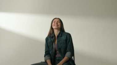 İnsani aşırı duygular yaratıcı reklam konsepti. Çekici kadın modelin olumlu ruh hali portresi. Esmer kadın, günlük kıyafetleriyle stüdyoda oturuyor ve kameraya gülüyor..