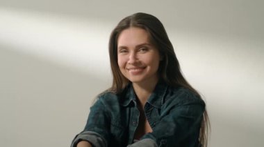 İnsani aşırı duygular yaratıcı reklam konsepti. Çekici kadın modelin olumlu ruh hali portresi. Esmer kadın, günlük kıyafetleriyle stüdyoda oturmuş kameraya poz veriyor ve gülümsüyor..