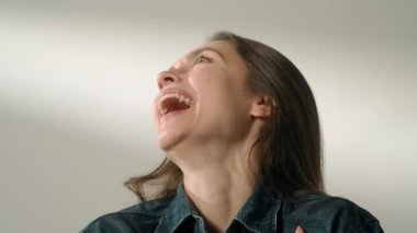 İnsani aşırı duygular yaratıcı reklam konsepti. Çekici kadın modelin olumlu ruh hali portresi. Esmer kadın, günlük kıyafetleriyle stüdyoda oturuyor ve geniş ve parlak bir şekilde gülüyor..