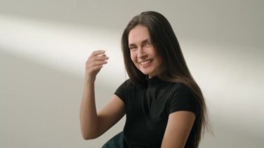 İnsani aşırı duygular yaratıcı reklam konsepti. Çekici kadın modelin olumlu ruh hali portresi. Esmer kadın gündelik kıyafetlerle stüdyoda oturuyor uzun saçlara dokunuyor ve gülümsüyor..