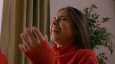 İnsan duyguları ve pozitiflik yaratıcı reklam konsepti. Keyfi yerinde güzel bir kadın modelin portresi. Kırmızı kazaklı esmer kadın stüdyoda oturuyor ve gülüyor ve el çırpıyor..