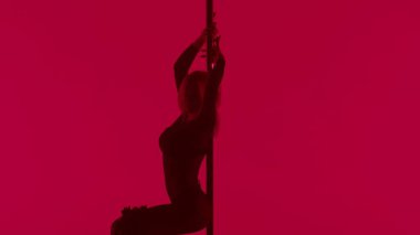 Modern dans tarzı ve koreografi yaratıcı konsepti. Stüdyodaki genç bayan dansçının portresi. Profesyonel striptizci kız direğin üzerinde dans ediyor, modern direk dansı gösteriyor, kırmızı neon arka plan.