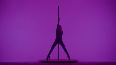 Modern dans tarzı ve koreografi yaratıcı konsepti. Stüdyodaki genç bayan dansçının portresi. Profesyonel striptizci kız direğin üzerinde dans ediyor, modern direk dansını gösteriyor, mor neon arka plan.