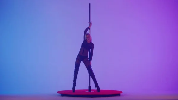 Modern dance style and choreography creative concept. Portrait of young female dancer in the studio. Professional pole dancer girl dancing on pylon, showing modern pole dance, pink purple background.