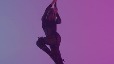 Modern dans tarzı ve koreografi yaratıcı konsepti. Stüdyodaki genç bayan dansçının portresi. Profesyonel striptizci kız direğin üstünde dans ediyor, modern direk dansı gösteriyor, pembe mor arka plan..