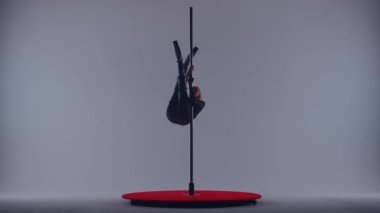 Siyah transparan tulumlu genç bir kadın direk dansı koreografisi yapıyor. Yüksek topuklu ayakkabılı dansçı. Stüdyoda gri arka planda erotik dans ediyor.