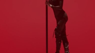 Modern dans tarzı ve koreografi yaratıcı konsepti. Stüdyodaki genç bayan dansçının portresi. Profesyonel striptizci kız direğin üzerinde dans ediyor, modern direk dansı gösteriyor, kırmızı neon arka plan.