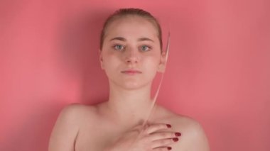 Pembe arka plan makyajsız çekici bir kızı gösteriyor. Görünüşte suyun altında yatıyor ve dikkatlice kameraya bakıyor, elini sürtüyor. Su dalgaları bozar, görüntüsünü bulanıklaştırır..