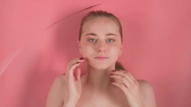 Pembe arka plan makyajsız genç ve çekici bir kızı gösteriyor. Görünüşte suyun altında yatıyor manikürlü bir elle yüzünü okşuyor ve kameraya bakıyor. Su dalgalar yaratırken.