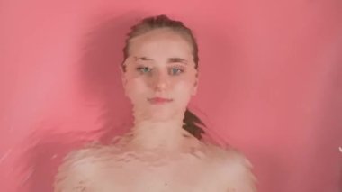 Pembe arka plan makyajsız genç ve çekici bir kızı gösteriyor. Görünüşte suyun altında yatıyor ve kameraya bakıyor. Su dalgaları onun görüntüsünü bozar ve bulanıklaştırır..