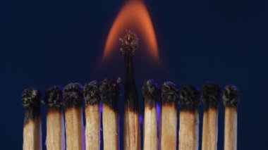 Bir sıra sönmüş kibrit. Bir orta saha maçı stüdyonun karanlık arkaplanını ışıkla aydınlatmaya devam ediyor. Bir makro çekimde yanan kibritler.