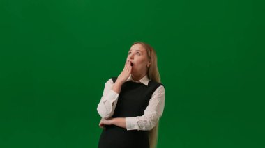 Sorun çözme konseptinde hayal gücü. Üzerinde yeşil arka planda izole edilmiş bir kadın portresi var. Ayakta duran kız yeni bir fikre kapılmış ve parmağını kaldırmış gülümsüyor, lamba yanıyor.