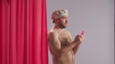 Su geçirmez kapaklı çıplak adam duş alırken akıllı telefon kullanıyor. Bir adam mavi bir stüdyoda pembe bir duş perdesinin yanında dikilirken akıllı telefondan mesaj yazmaya konsantre oluyor.