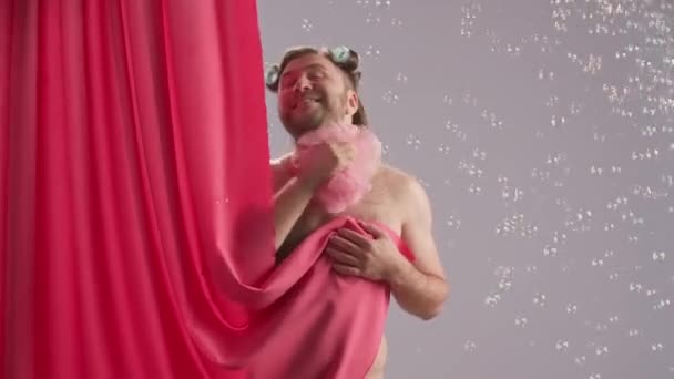彼の頭にカーラーが付いているおかしい男は ルーファーをマイクとして使用して歌うピンクのシャワーカーテンで覆われた 石鹸の泡に囲まれた青い背景にスタジオでシャワーを浴びる漫画家 — ストック動画
