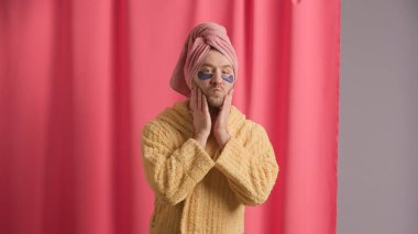 Bir adam duştan sonra yüzüne dokunuyor teninin keyfini çıkarıyor ve hava öpücüğü yolluyor. Sarı cüppeli bir adam, kafasında havlu ve gözlerinin altında pembe duş perdesine karşı hidrojel yamalar.