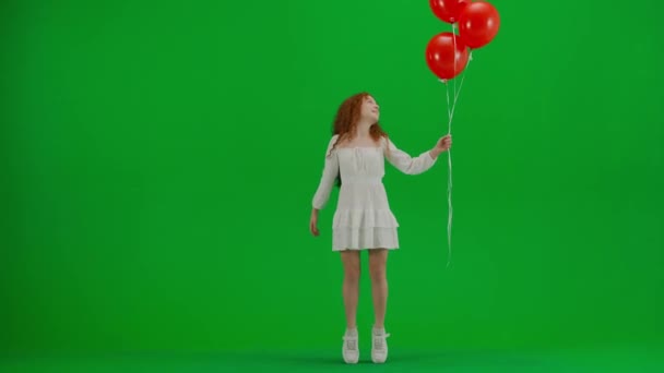 子どもたちクリエイティブなコンセプト スタジオの小さな女の子の肖像画 クロマキーグリーンスクリーンの赤いヘリウム風船の白いドレスの小さな女の子は 笑顔を見上げて先端のつま先に立って隔離された背景 — ストック動画