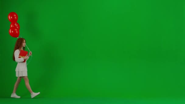 儿童创意概念 工作室里小女孩的画像 小女孩穿着白色的衣服 红色的氦气气球挂在彩色键绿色的屏幕上孤立的背景步行礼品盒 喜形于色 — 图库视频影像