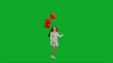 Çocukların yaratıcı konsepti. Stüdyoda küçük bir kızın portresi. Krom anahtar üzerinde kırmızı helyum balonları olan beyaz elbiseli küçük bir kız. Yeşil ekran izole edilmiş arka plan. Dönüp kameraya bakıyor.