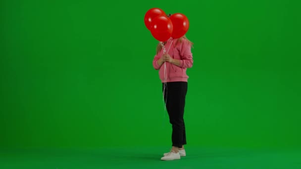 子どもと子育てのクリエイティブコンセプト スタジオで女性モデルの肖像画 立って クロマキーグリーンスクリーンで赤いヘリウム風船の背後に彼女の顔を隠す女性 — ストック動画