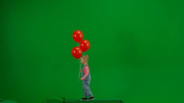 Çocukların yaratıcı konsepti. Stüdyoda küçük bir kızın portresi. Kot pantolonlu küçük kız ve kırmızı helyum balonlu at kuyruklu yeşil ekran krom üzerinde yürüyen izole edilmiş arka plan,.