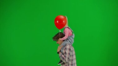 Çocukların yaratıcı konsepti. Stüdyoda küçük bir kızın portresi. Omzunda kırmızı balon olan ve krom anahtar yeşil ekranda yürüyen bir adam..