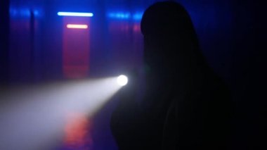 Terk edilmiş yerler ve boş binalar yaratıcı reklam konsepti. Karanlık koridorda neon ışıklı bir kadın portresi. Elinde fener olan bir kadın koridorda duruyor ve etrafı inceliyor..