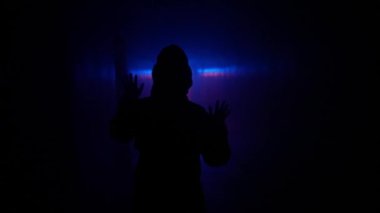 Terk edilmiş yerler ve boş binalar yaratıcı kavramlar. Koridordaki neon ışıkta siluet portresi. Kimyasal koruma giysisi giyen biri karanlık koridorda dikkatli bir şekilde yürüyor, duvara dayanıyor.