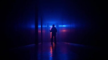 Terk edilmiş yerler ve boş bina konsepti. Koridorda neon ışıklı bir siluet portresi. Kimyasal koruma giysisi giyen biri karanlık koridorda dikkatli bir şekilde yürür ve alçak kameraya bakar.