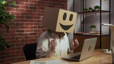 İş hayatı ve ofis günlük yaratıcı reklam konsepti. Kafasında emoji olan karton kutuda bir kadın portresi. İşçi masada oturuyor dizüstü bilgisayarla çalışıyor, el hareketlerini kazanıyor..