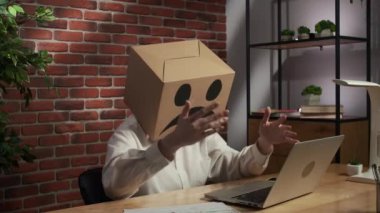 İş hayatı ve ofis günlük yaratıcı reklam konsepti. Kafasında emoji olan karton kutuda bir kadın portresi. Masada oturan işçiler dizüstü bilgisayarda çalışıyor, hayal kırıklığına uğramış ifadeler.