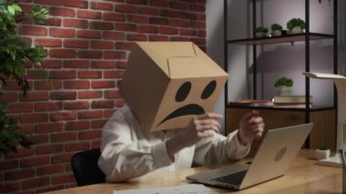 İş hayatı ve ofis günlük yaratıcı reklam konsepti. Kafasında emoji olan karton kutuda bir kadın portresi. Masa başı çalışanı dizüstü bilgisayarda çalışır, üzgün surat fikir değişiklikleri mutlu yüz yapar..