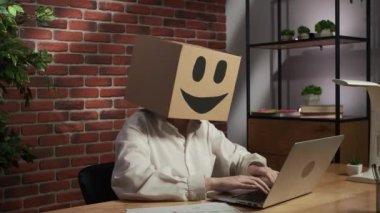 İş hayatı ve ofis günlük yaratıcı reklam konsepti. Kafasında emoji olan karton kutuda bir kadın portresi. Masadaki işçiler dizüstü bilgisayarda çalışırken mutlular, üzgün ifadeye geçiyorlar..