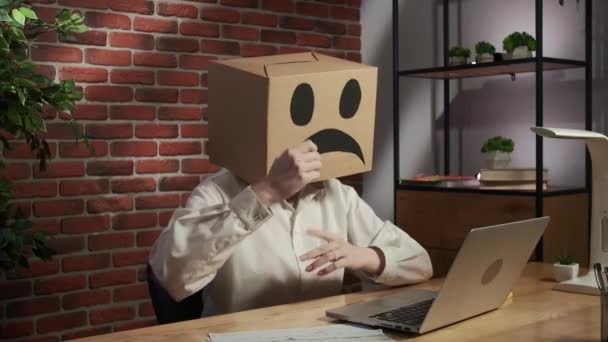 ビジネスライフとオフィスの日常的なクリエイティブ広告コンセプト 頭に絵文字が入った段ボール箱の女性の肖像 机の悲しい顔に座っている労働者は頭を保持するテーブルの上に拳を打つ — ストック動画