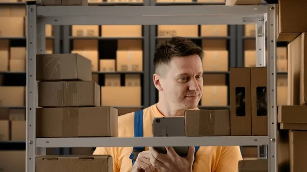 Business warehouse and logistics creative advertisement concept. Portrait of male working in storage. Man storekeeper standing near rack with boxes, checking good writing on tablet, positive face.