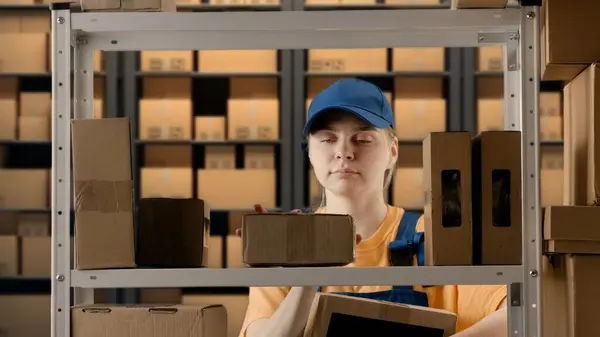Business warehouse and logistics creative advertising concept. Portrait of a female model working in a warehouse. Uniformed warehouse girl lays on a shelf cardboard box