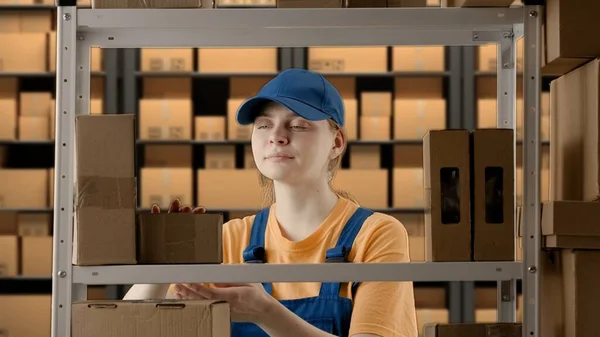 Business warehouse and logistics creative advertising concept. Portrait of a female model working in a warehouse. Uniformed warehouse girl lays on a shelf cardboard box