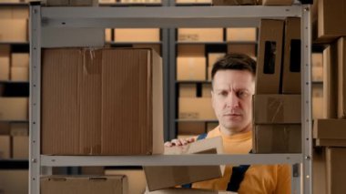İş deposu ve lojistik yaratıcı reklam konsepti. Depoda çalışan erkek portresi. Rafların yanında bir depo dolusu kutu bulunduruyor raflara paketler koyuyor ve malları düzenliyor..