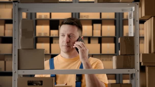 商务仓储和物流创意广告理念 男性在储藏室工作的肖像 男店主站在架子旁边 一边用智能手机大喊着 一边满脸沮丧地看着包装 — 图库视频影像