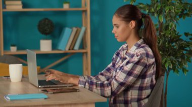 Evinde dizüstü bilgisayarla çalışan ve kahve içen bir kadını orta ölçekte çekmiş. Genç bir kadın programcı, daktilo eden bir iş kadını, bir proje üzerinde çalışıyor. Uzak iş, modern yaşam tarzı.