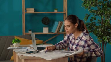 Ofisinde çalışan bir kadını orta ölçekli çekte yakalamış. Genç mimar binanın planlarını karşılaştırıyor ve bilgisayarına veri yerleştiriyor. Uzak iş, modern yaşam tarzı.