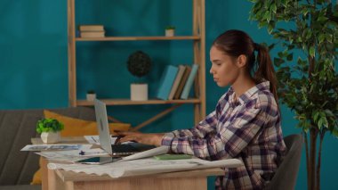 Ofisinde çalışan bir kadını orta ölçekli çekte yakalamış. Genç mimar binanın planlarını karşılaştırıyor ve bilgisayarına veri yerleştiriyor. Uzak iş, modern yaşam tarzı.