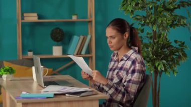 Ofisinde çalışan bir kadını orta ölçekli çekte yakalamış. Genç iş kadını grafikleri ve grafikleri inceliyor ve onları agresif bir şekilde havaya fırlatıyor. Uzak iş, modern yaşam tarzı.