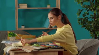 Ofisinde çalışan bir kadını orta ölçekli çekte yakalamış. Genç tasarımcı projesinin renk paletlerini karşılaştırarak bilgisayarına veri ekliyor. Uzak iş, modern yaşam tarzı.