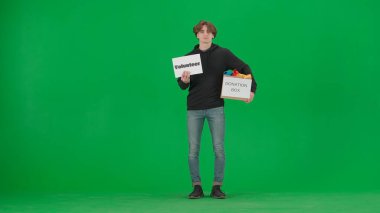 Bir adam, üzerinde gönüllü yazan bir poster ve kıyafetlerle dolu bir bağış kutusu tutuyor. Yeşil ekrandaki erkek gönüllü. İnsanlara yardım etmek