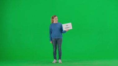 Bir kadın elindeki pankartı işaret ederek vejetaryen ol diyor ve onaylıyor. Stüdyoda yeşil ekranda genç bir kadın aktivist.