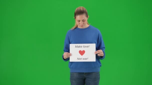 一个年轻的女人拿着标语牌 上面写着 不要让爱情成为战争 在绿色屏幕上的工作室里的女性积极分子们正在接近 反战口号 呼吁和平 — 图库视频影像
