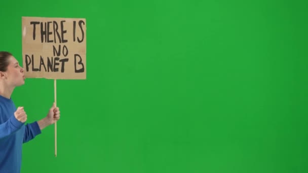 一个尖叫的女权运动者拿着标牌说没有行星B的侧视图 一个拿着标语牌的女性抗议者走在绿色的屏风上 拯救地球 全球变暖和气候 — 图库视频影像