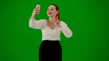Modern iş kadını yaratıcı reklam konsepti. Krom anahtar yeşil ekranda çekici ofis kızı portresi. Etekli bir kadın yürüyor ve akıllı telefondan selfie çekiyor, gülümsüyor..